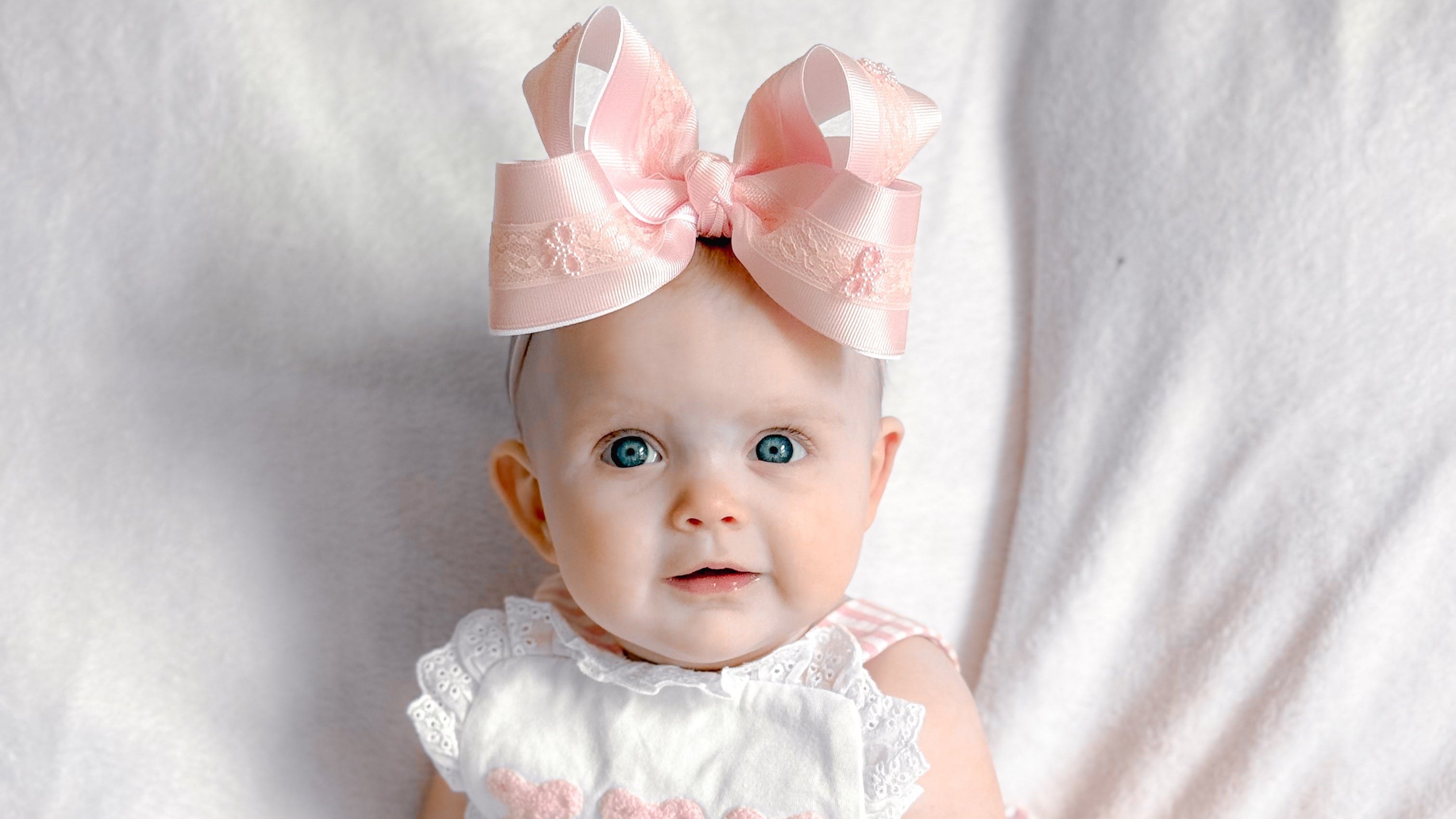 Baby wearing a pink outfit with a large bow on a white background